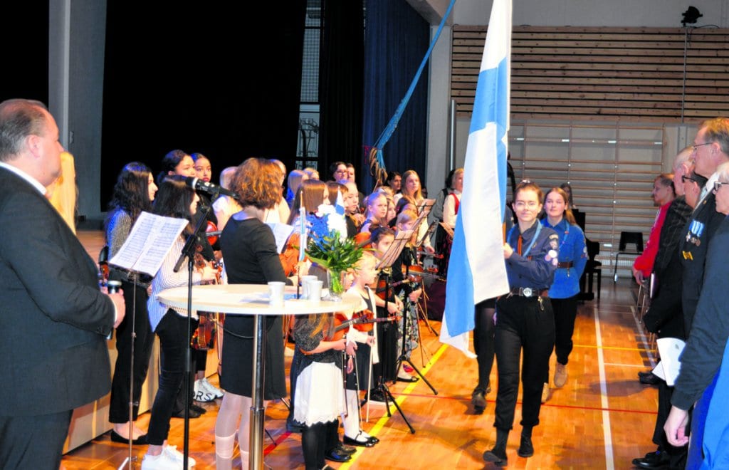 Kuvassa Vuosaaren Vesipääskyjen partiolaiset saattavat Suomen lipun saliin yleisön ja Vuosaaren musiikkikoulun jousiorkesterin todistaessa tapahtumaa. 