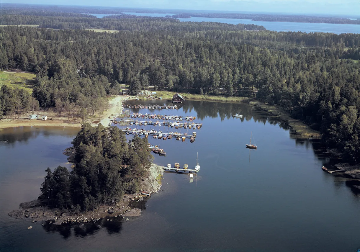 Kuva vuodelta 1972 Uutelan Mustalahden venesatamasta. Uuden asuinalueen myötä nimi Mustalahti vaihtui myöhemmin Aurinkolahdeksi. VUK:n venelaiturit olivat tuolloin lahden toisella reunalla, sa- moin kahvila Kampela oli hieman lännempänä nykyisesti paikastaan. Vanhan kahvilan kohdilla on nyt Uutelan kanavan suu. Uimaranta oli tuolloin melko lyhyt. Kuva: Helsingin kaupunginmuseo, Studio B. Möller 1972