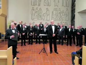 Helsingin Lauluveljet adventtikonsertissa 27.11. viimeistä sijaa myöten täyttyneessä Vuosaaren kirkossa. Edessä keskellä kuoronjohtaja Teppo Lampela, vasemmalla puhumassa Unto Palminkoski.