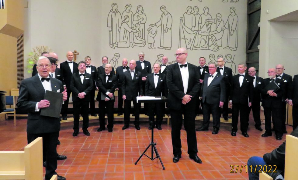 Helsingin Lauluveljet adventtikonsertissa 27.11. viimeistä sijaa myöten täyttyneessä Vuosaaren kirkossa. Edessä keskellä kuoronjohtaja Teppo Lampela, vasemmalla puhumassa Unto Palminkoski.