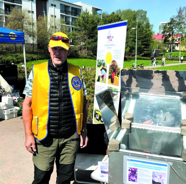 Kuvassa lion Heikki Saarinen esittelee aurinkokeittimen toimintaa. Keittimen lämpötila nousi hetkessä noin 120 asteeseen ja keittimessä olleet perunat, porkkanat ja grillimakkarat kypsyivät helposti.