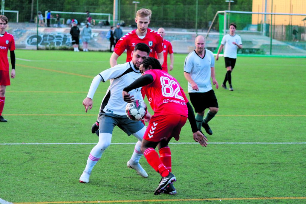Gilla FC:ssä pelaava räppäri Ege Zulu (oikealta nimeltään Eugene Mokulu) taistelee pallosta selin kameraan. Tilannetta seuraa taustalla hänen seurakaverinsa tubettaja Roni Bäck. 