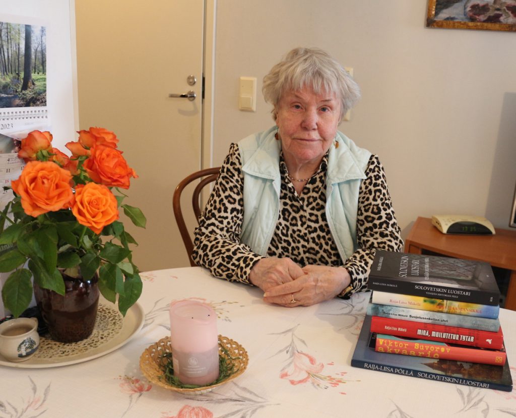 Raija-Liisa Mäkelä kotonaan Rastilankalliossa. Pöydällä on kaikki Mäkelän kirjoittamat kirjat sekä hänen suomentamansa Viktor Suvorovin romaani Akvaario, joka kertoo Venäjän sotilaallisesta tiedustelusta GRU:sta.