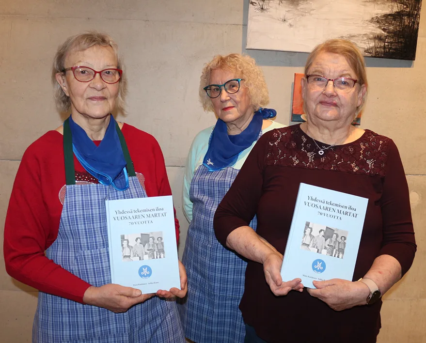 Edessä vasemmalla kirja kädessään Marttojen puheenjohtaja Maire Karttunen ja oikealla sihteeri Sirkka Rinne. Keskellä taustatyössä myös mukana ollut entinen puheenjohtaja Lili Järvinen.