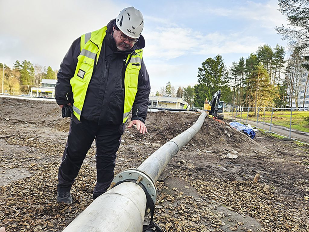 Työmaapäällikkö Mika Huovinen tarkastaa putkea, jonka kautta imuruopattu liete siirtyy geotuubikentälle. Polymeeriliuoksen lisäyspisteestä säädellään veden erottumista lietteestä. Ruoppauksen aikana geotuubikenttää valvoo aina yksi työntekijä toisen ruopatessa lampea.                           Kuva: Anna-Leena Pyykönen