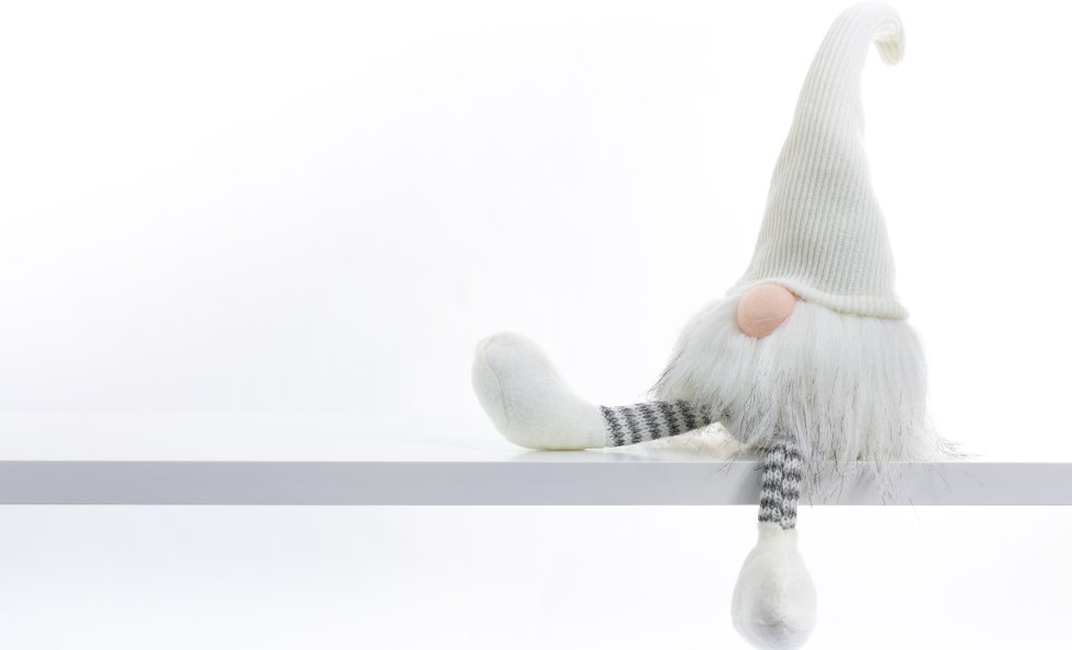 Gnome a Christmas elf is relaxed and sitting on white shelf with hanging leg