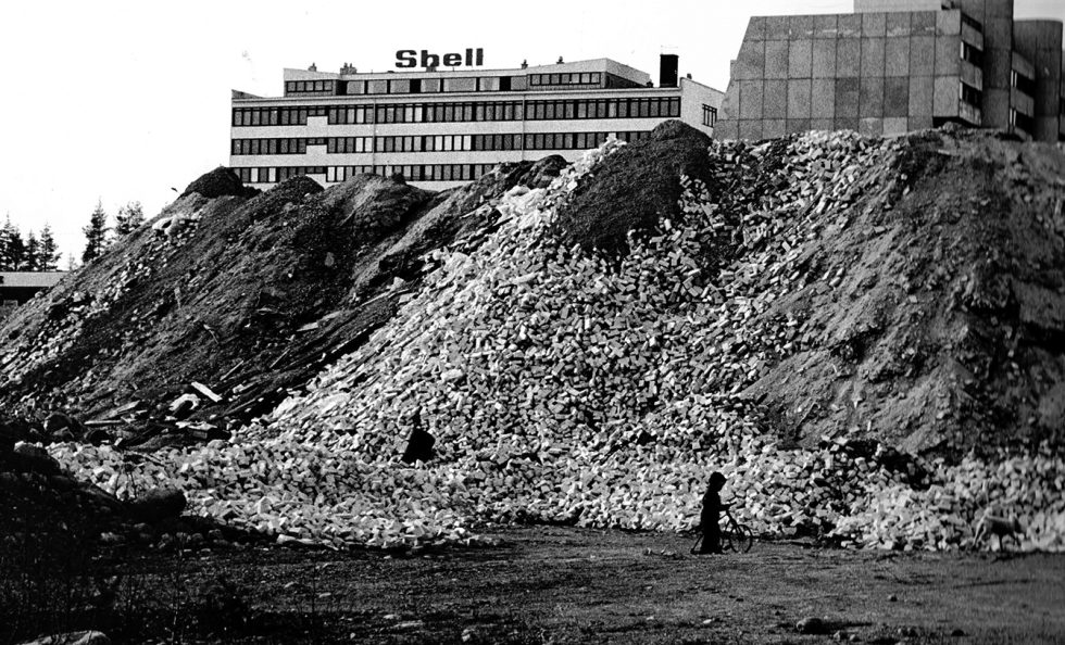 Vuosaarentie 3:n kohdalla sijaitsi rakennusjätteen kaatopaikka vielä 1970-luvulla. Takana Ulappasaarentie 4:ssä sijaitsi Shellin pääkonttori ja oikealla Ulappasaarentie 1:n terassitalo. Terassitalot valmistuivat vuosina 1969–71. Vuokeskus eli Raken ostari ja kirjasto pilkottavat kuvan vasemmassa reunassa. Kuva: Vuosaari-lehden arkisto